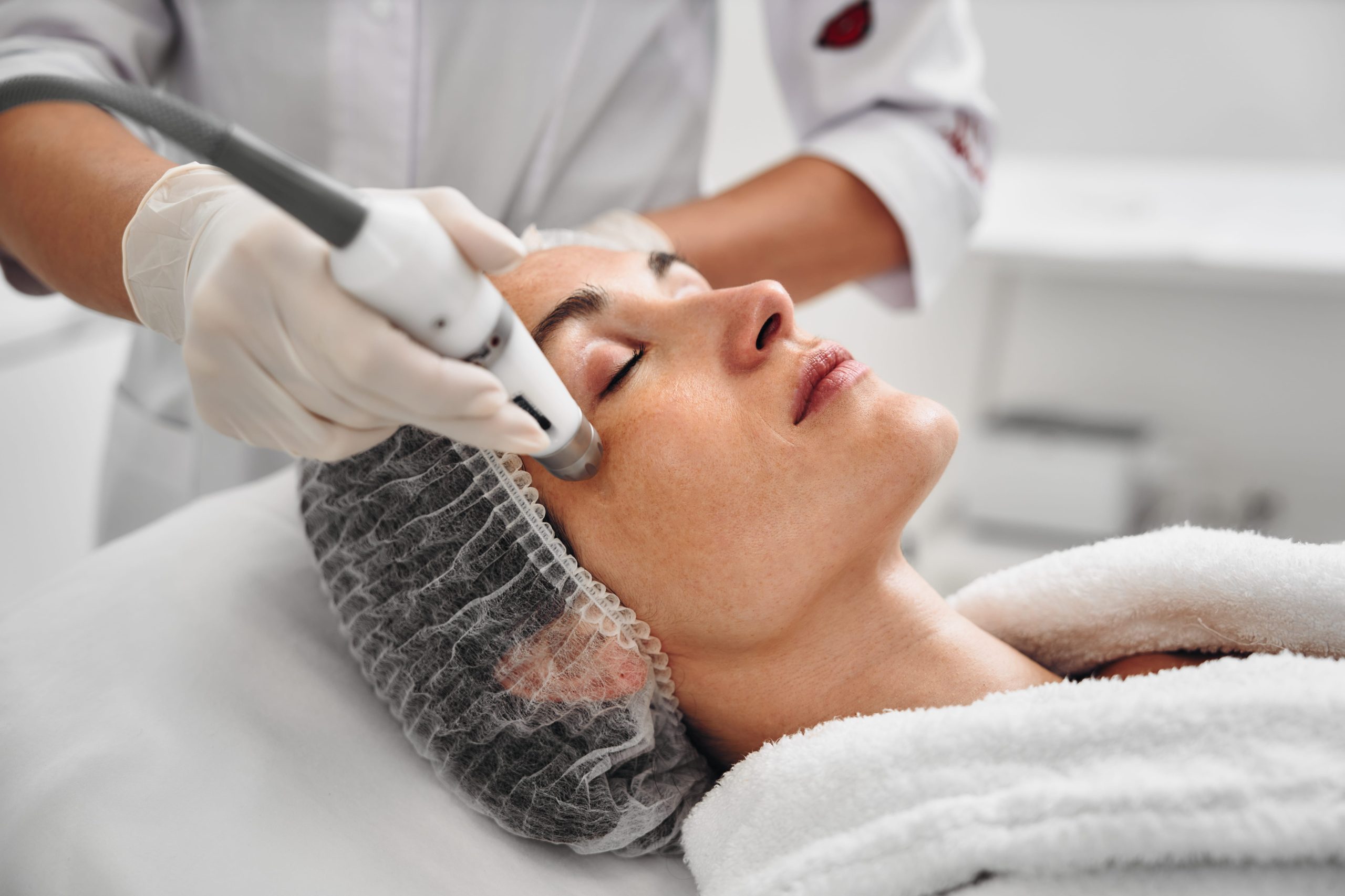 Mulher recebendo tratamento com laser dermatológico em clínica médica durante o inverno.